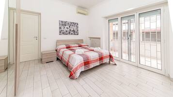 Un dormitorio con cama, un banco, un radiador y una puerta corredera de cristal a un balcón.