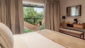 A bedroom with a bed, a hammock, a bedside table with a lamp, and a view of greenery outside. - Hotel Alto Monte (Chiguir í Arriba)