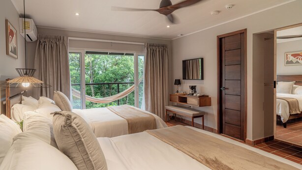 A bedroom with two beds, a hammock, a ceiling fan, a window with curtains, and a door leading to another room. - Hotel Alto Monte (Chiguirí Arriba)