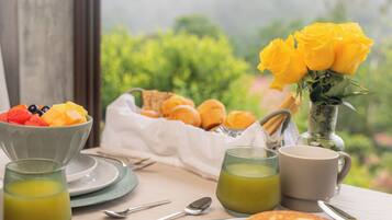 Una mesa de desayuno con panqueques, fruta y un ramo de rosas amarillas.