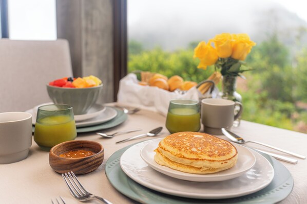 A breakfast setting with pancakes, fruit, croissants, and a view of greenery. - Hotel Alto Monte (Chiguirí Arriba)