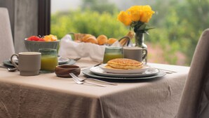 A breakfast table with a plate of pancakes, a bowl of fruit, a cup of coffee, and a glass of orange juice. - Hotel Alto Monte (Chiguirí Arriba)