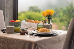 A breakfast table with a plate of pancakes, a bowl of fruit, a cup of coffee, and a glass of orange juice.
