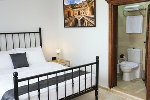 Une chambre à coucher avec un lit, une table de chevet avec une lampe, une salle de bain avec des toilettes et un tableau encadré au mur.
