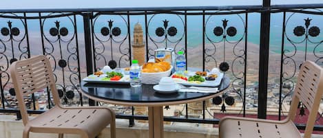 A balcony with a table set for a meal, two chairs, a lamp, and a view of a distant building.