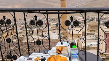 A table with a meal set on a balcony overlooking a cityscape with a prominent tower.