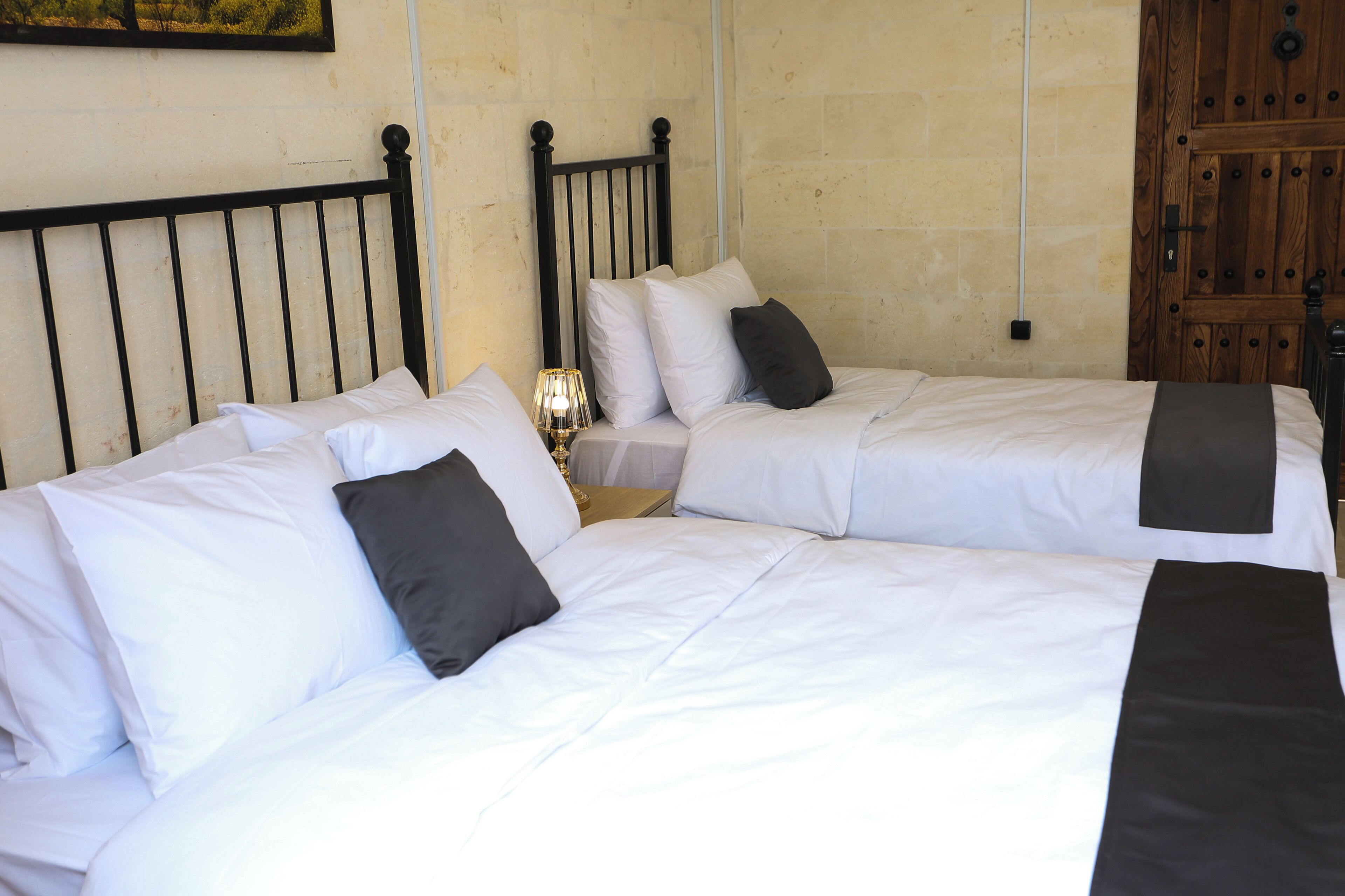 A double bed with white bedding and a black headboard, a bedside table with a lamp, and a wooden wardrobe.