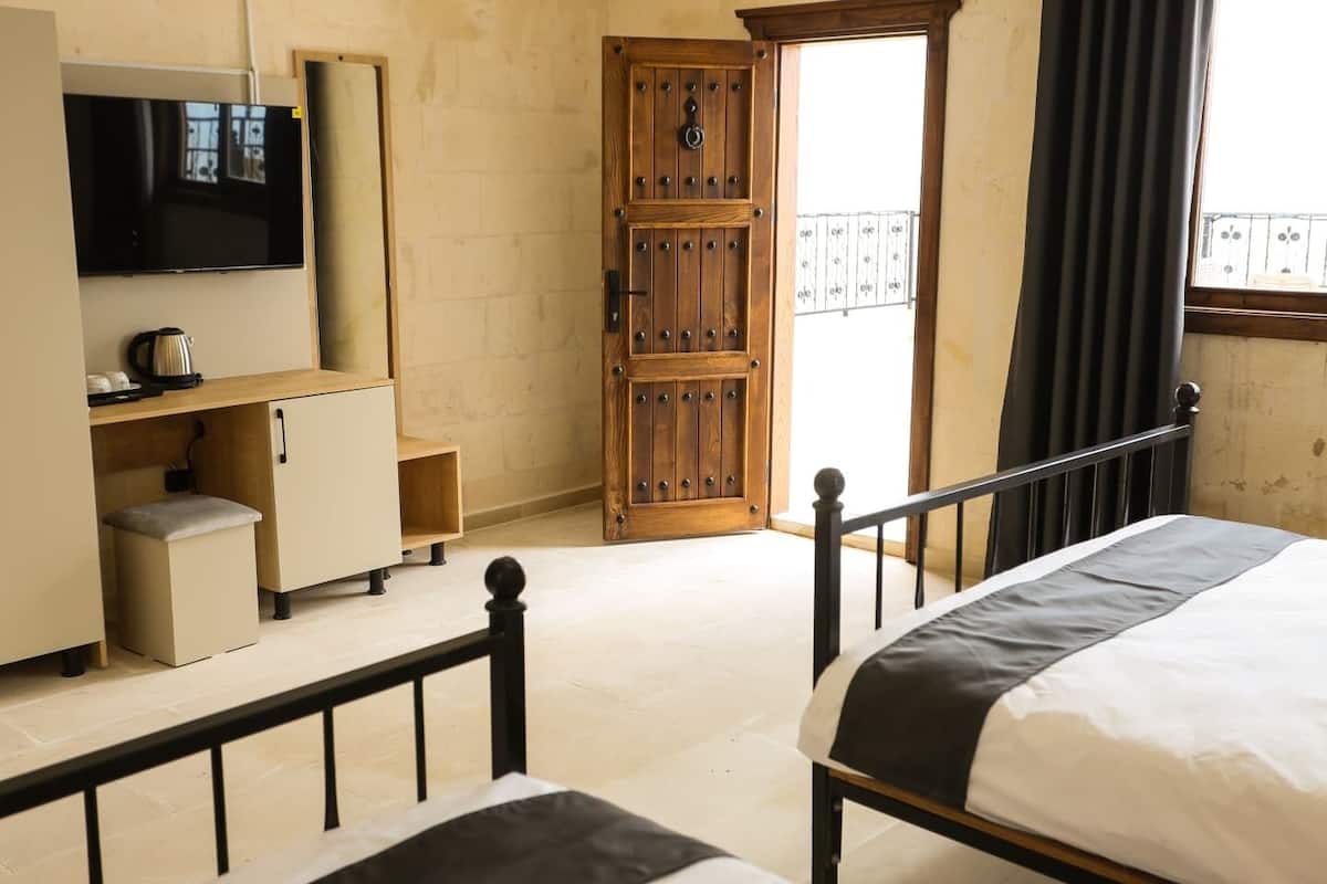 Un dormitorio con cama, televisor, armario de madera, una mesita con tetera y puerta al balcón.