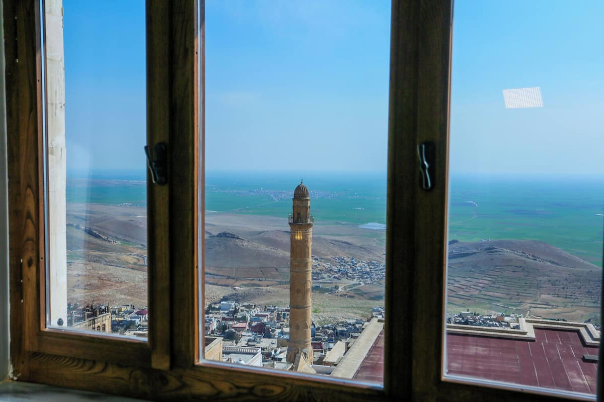Vista a través de una ventana con marco de madera, un horizonte urbano lejano y una torre destacada.