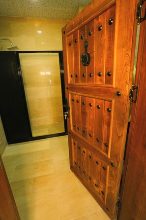 Une porte en bois ornée de clous métalliques et dotée d’un trou de serrure, qui donne sur une salle de bain carrelée avec un espace douche.