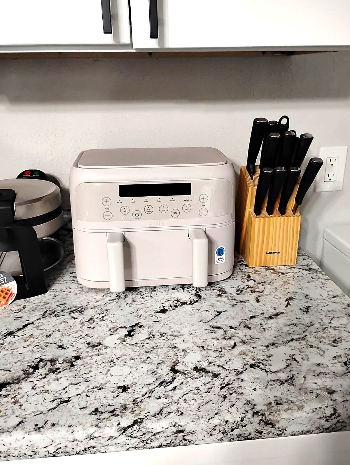 Una cocina con encimera blanca, una plancha para gofres y un bloque de cuchillos.