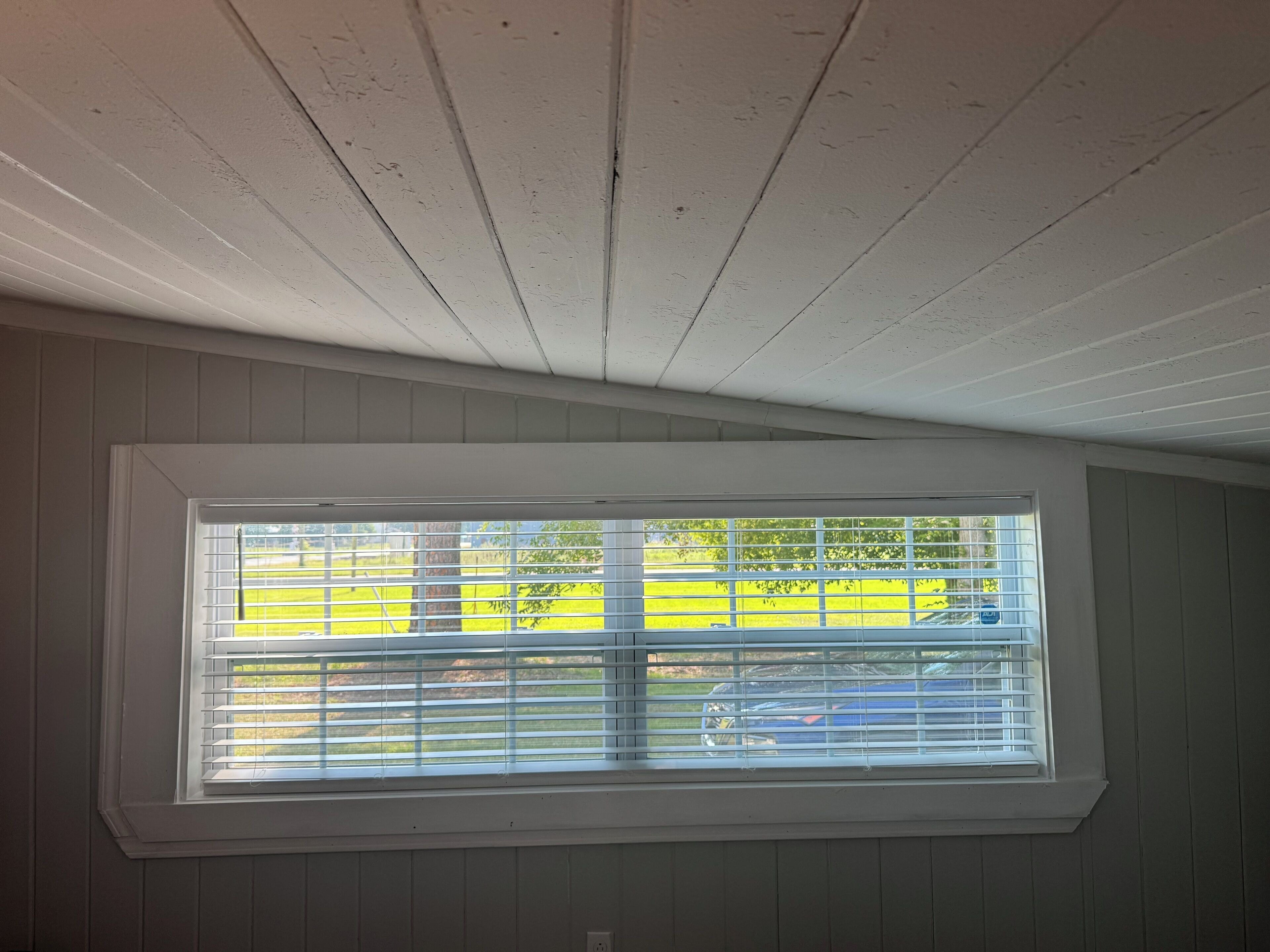 Ein Zimmer mit Fenster, weißer Decke und Holzwänden.