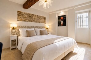 Ein Schlafzimmer mit einem großen Bett, zwei Nachttischen, einer Steinwand, einem Deckenventilator und einem Fenster mit Gitter.