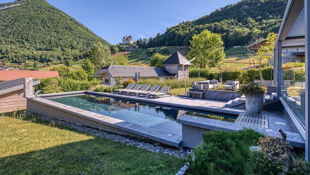 Una piscina amb gandules, una casa moderna i un paisatge de muntanya al fons.