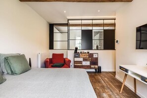 Une chambre à coucher avec un lit, une chaise rouge, un bureau blanc et un miroir.