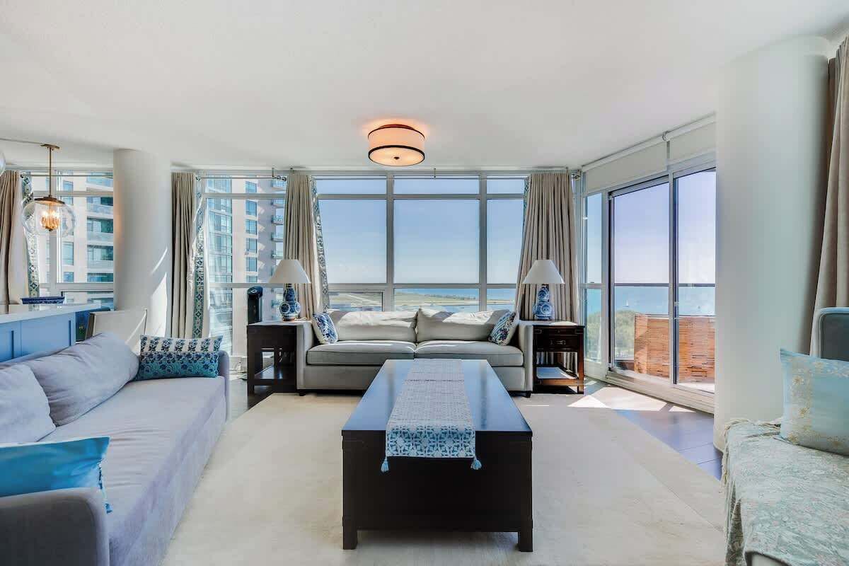 Bright and spacious living room with floor-to-ceiling windows, comfortable seating, and stunning lake views.