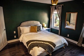 A bedroom with a bed, a nightstand, a window with curtains, and a mirror on the wall. - Cozy 2BR Townhouse w/ 2 Workspaces & WiFi (Toronto)