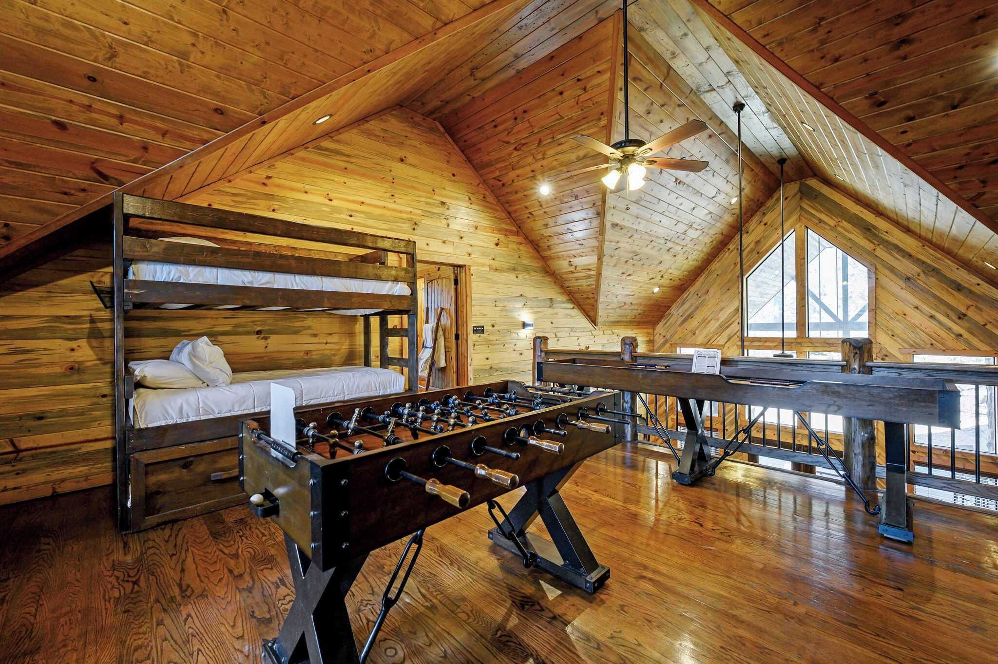 A loft-style room with wooden walls, a foosball table, a bunk bed, and a ceiling fan.
