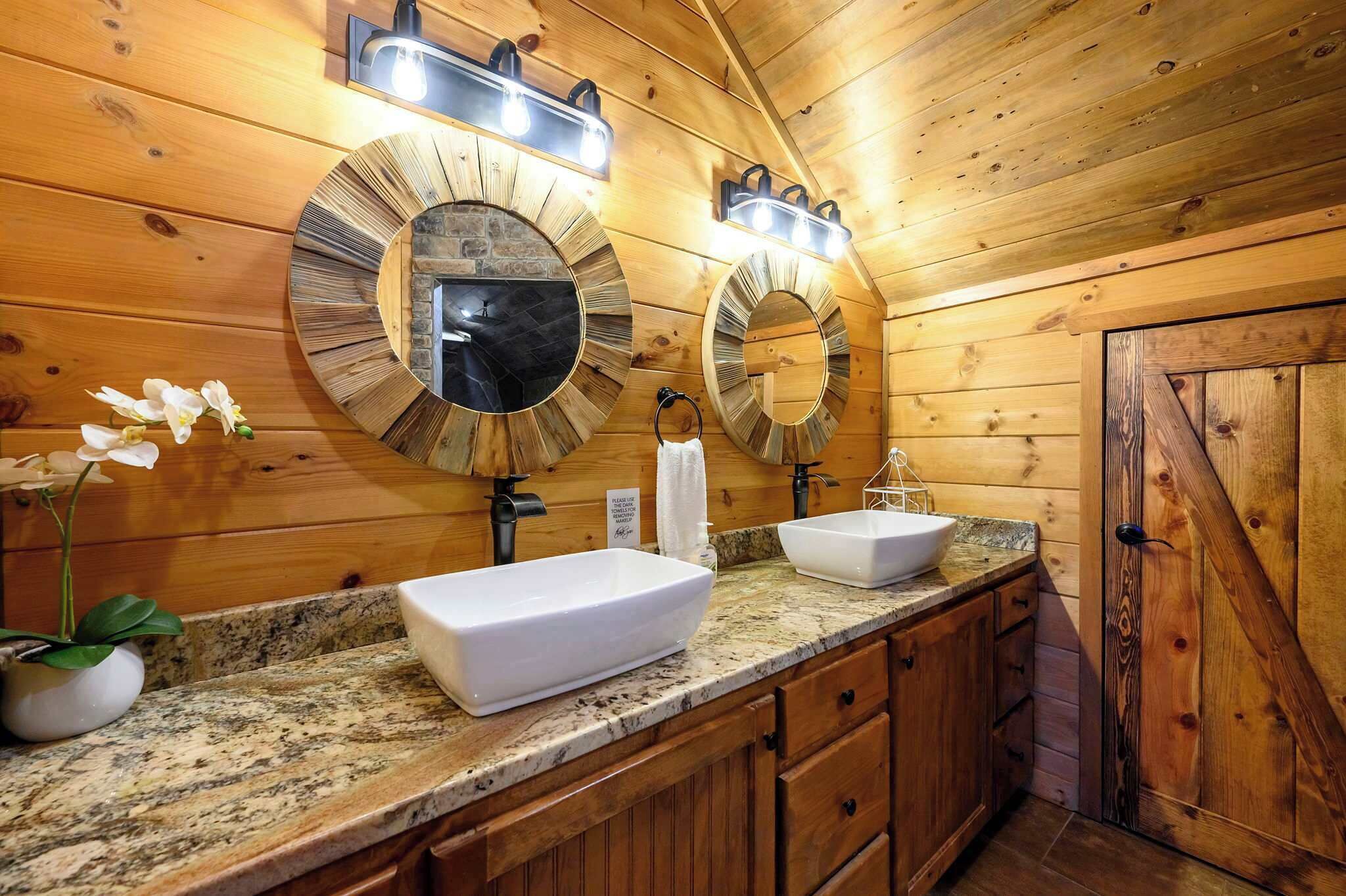 Ein Badezimmer einer Holzhütte mit zwei Waschbecken, runden Spiegeln und einem Handtuchhalter.