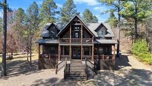 A two-story log cabin with a balcony, a front porch, and a staircase leading to the entrance. - Twisted Mane - Prime Location - Family Friendly (Broken Bow)