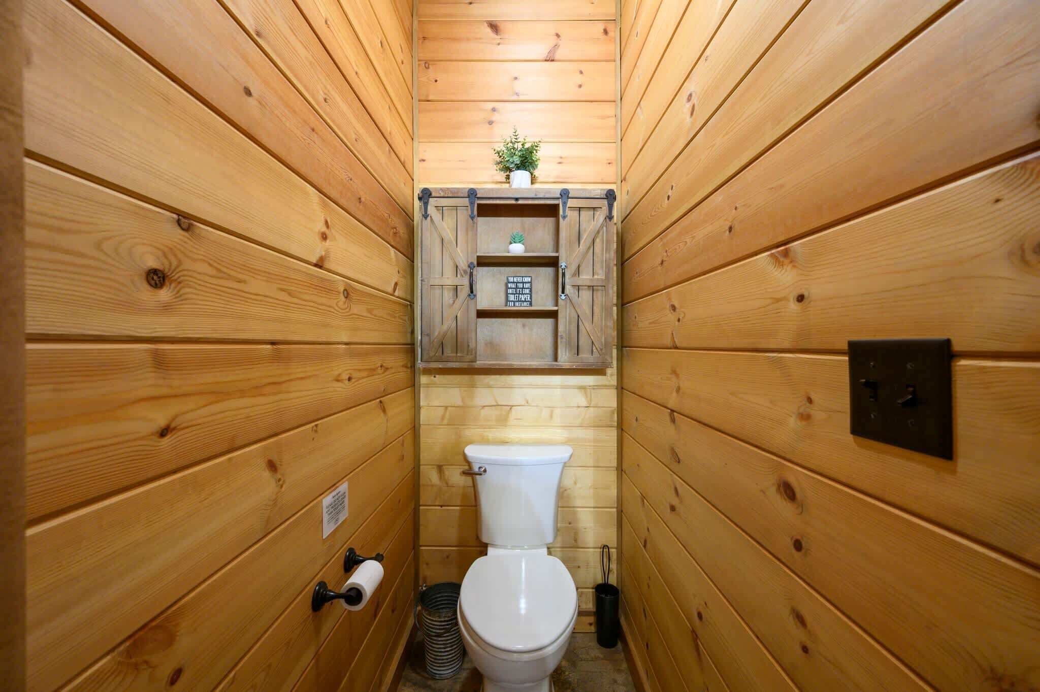 Een badkamer met houten lambrisering, een toilet, een klein plankje met een plant erop, en een bord boven het toilet.