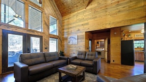 A spacious living room with leather sofas, a coffee table, and large windows. - Twisted Mane - Prime Location - Family Friendly (Broken Bow)
