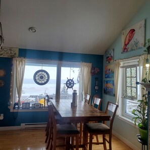 A dining area with a view of the sea, nautical decorations, and a large window with curtains.
