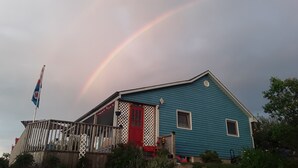 Et hus med røde døre, blå facade og et synligt regnbue på himlen.