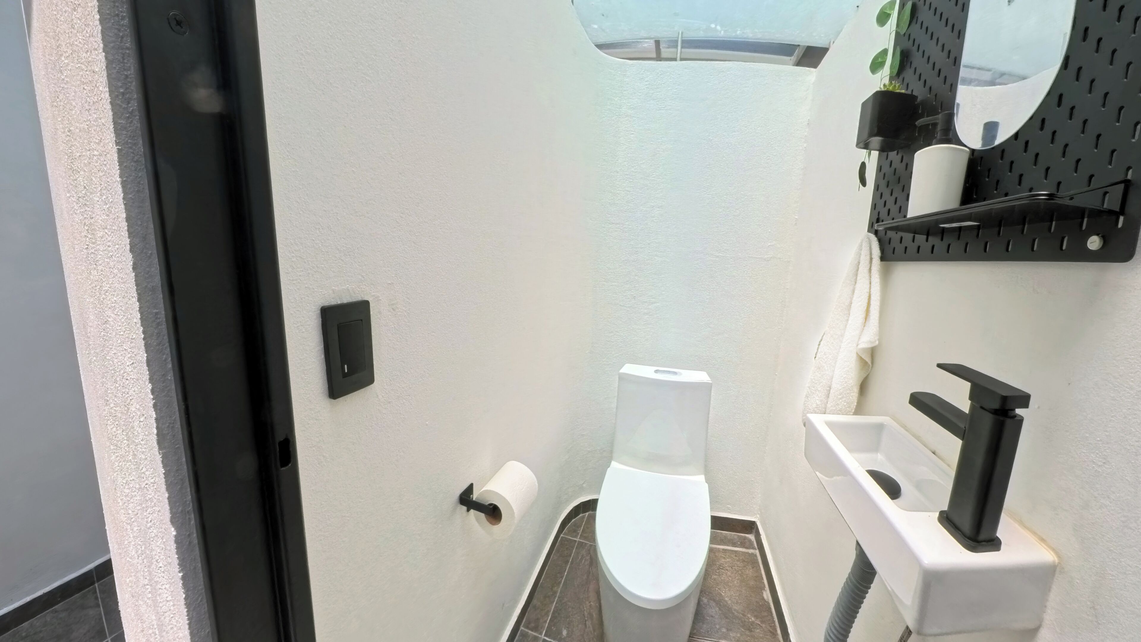 A compact bathroom with a toilet, a sink, a towel rack, and a small shelf with toiletries.