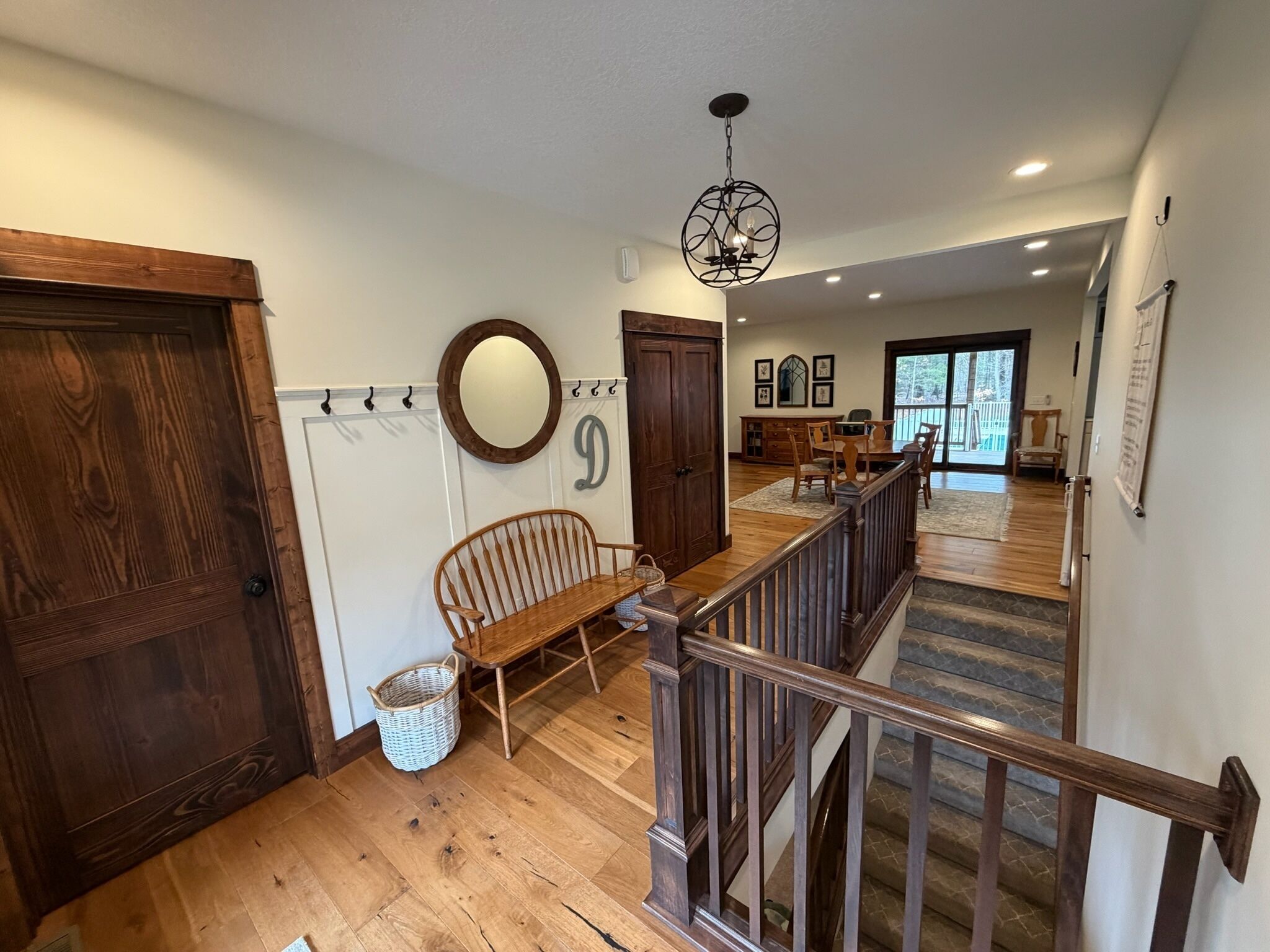 A wooden-floored hallway with a bench, a staircase, and a dining area with a table and chairs.