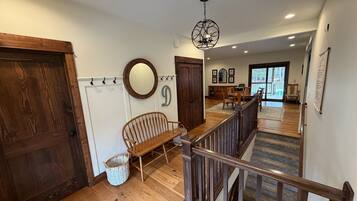 A wooden-floored hallway with a bench, a staircase, and a dining area with a table and chairs.