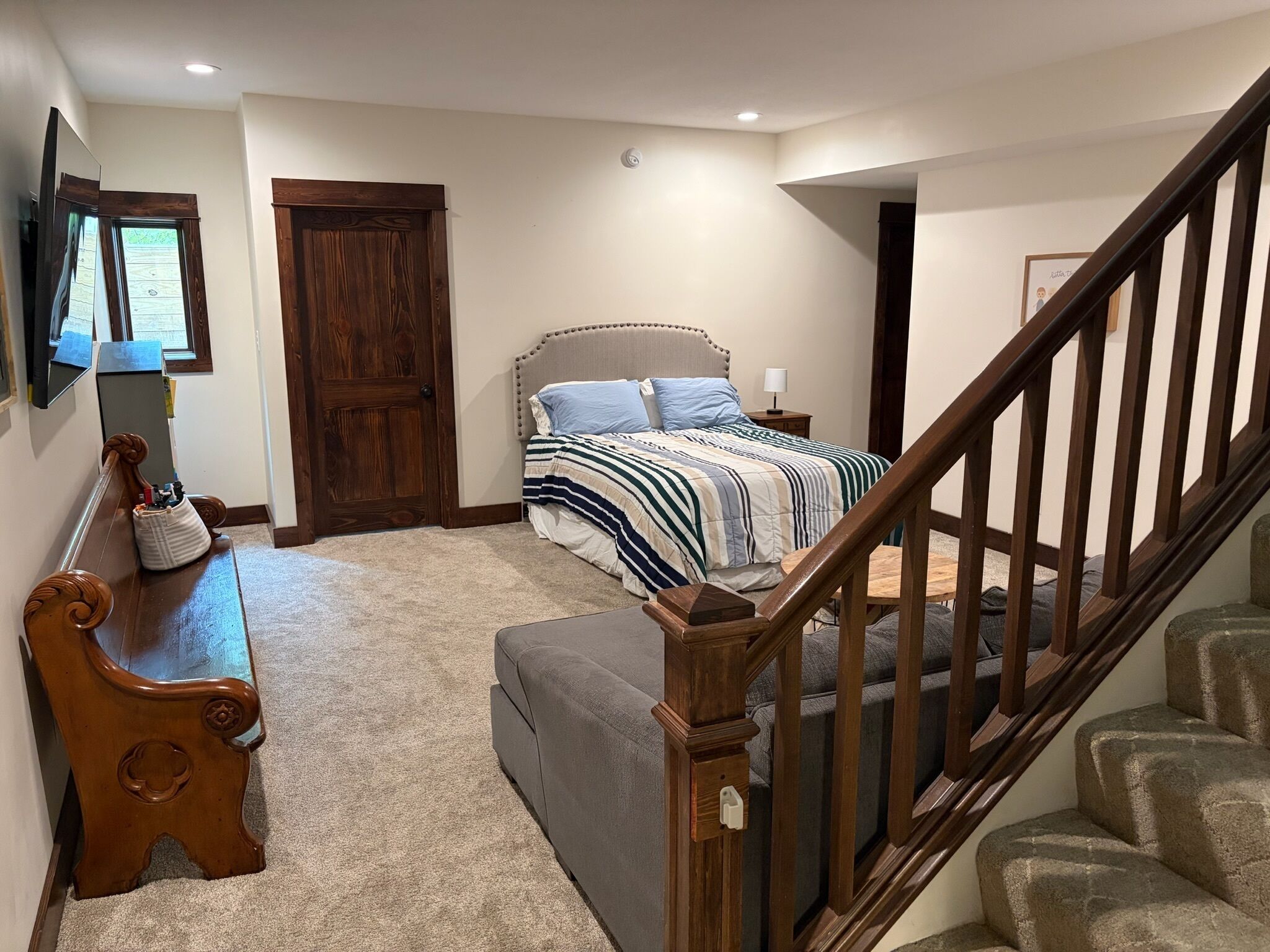 A bedroom with a bed, a wooden bench, a staircase, and a door.