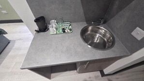 Eine Küche mit Spüle aus Edelstahl, einer Kaffeemaschine und einer grünen Ablage mit Tassen und einer Tasche Taschentücher.
