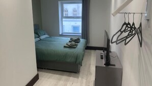 Un dormitorio con una cama, una ventana, un televisor y un perchero.
