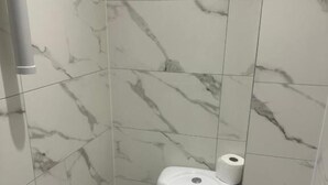 Un baño pequeño y moderno con un inodoro, un rollo de papel higiénico y un secador de manos.