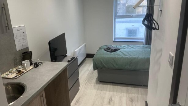 Una habitación de hotel compacta con kitchenette, una cama, un ventanal y vistas al exterior.