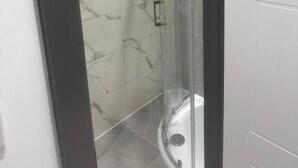 Una ducha con paredes de vidrio y diseño curvo, azulejos de mármol blanco en las paredes y suelo oscuro.