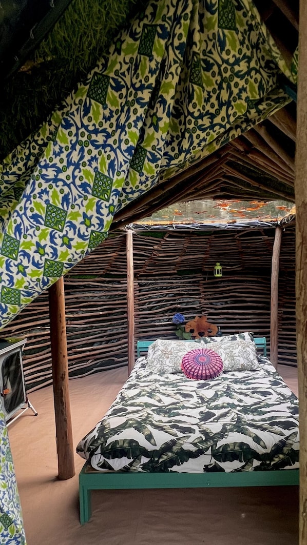 Una habitación con cama, un banco de madera y techo de paja.