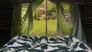 Ein Zimmer mit einem Bett, grünen Vorhängen mit Muster und Blick auf einen Garten.