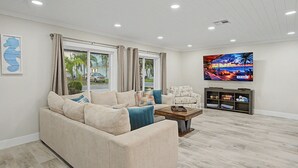Ein Wohnzimmer mit einem beigefarbenen Sofa, einem Couchtisch, einem Fernseher und Blick ins Freie.