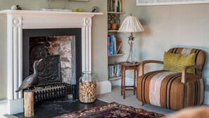A living room with a fireplace, a bookshelf, a lamp, a chair, and a patterned rug. - 3 Monteagle - sleeps 6 guests  in 3 bedrooms (Wells-next-the-Sea)
