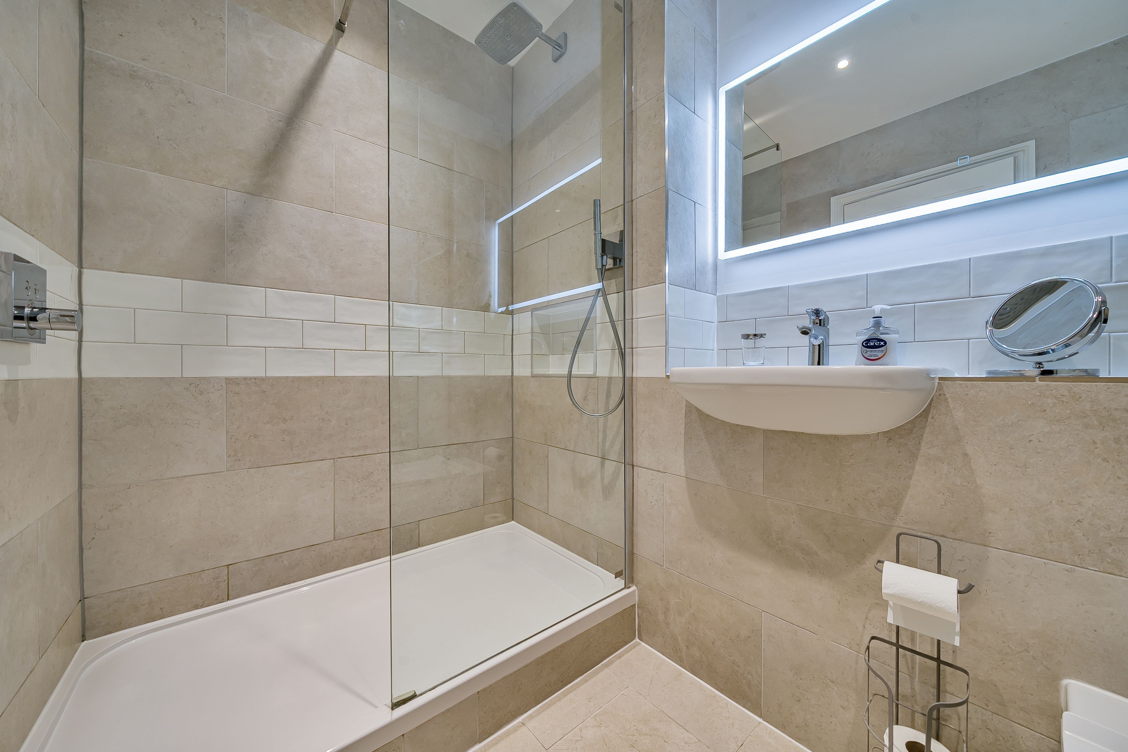 Un baño moderno con ducha de vidrio, un lavabo blanco y un espejo sobre él.