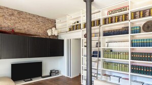 Una sala de estar con pared de ladrillo, televisor de pantalla plana, estantería y chimenea.