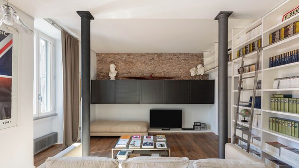 Una sala de estar con pared de ladrillo, un sofá, una mesa de centro con libros, un televisor y una estantería.