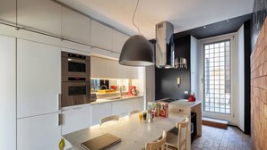 Una cocina moderna con armarios blancos, electrodomésticos de acero inoxidable, una isla central con sillas y un ventanal grande.
