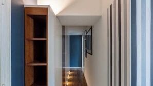 Un pasillo estrecho con un estante empotrado de madera a la izquierda, una pared azul a la derecha y una serie de cuadros enmarcados en la pared.