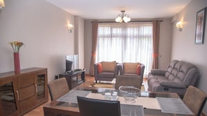 A living room with a sofa, armchair, and dining table. - Westlands 1BR w/a Pool & Gym • Walk to Sarit (Nairobi)