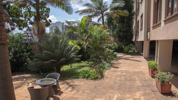 A paved courtyard with wicker furniture, potted plants, and a pathway leading to a building. - Westlands 1BR w/a Pool & Gym • Walk to Sarit (Nairobi)