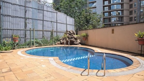 A swimming pool with a tiled deck, a rock feature, and potted plants. - Westlands 1BR w/a Pool & Gym • Walk to Sarit (Nairobi)