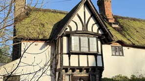 A traditional half-timbered house with a steeply pitched roof, a visible chimney, and a window with a white frame.